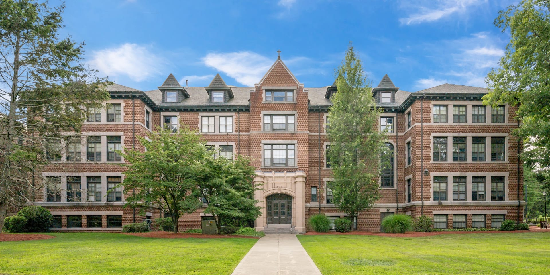 Brick academic building with cross on roof and tree-lined walkway