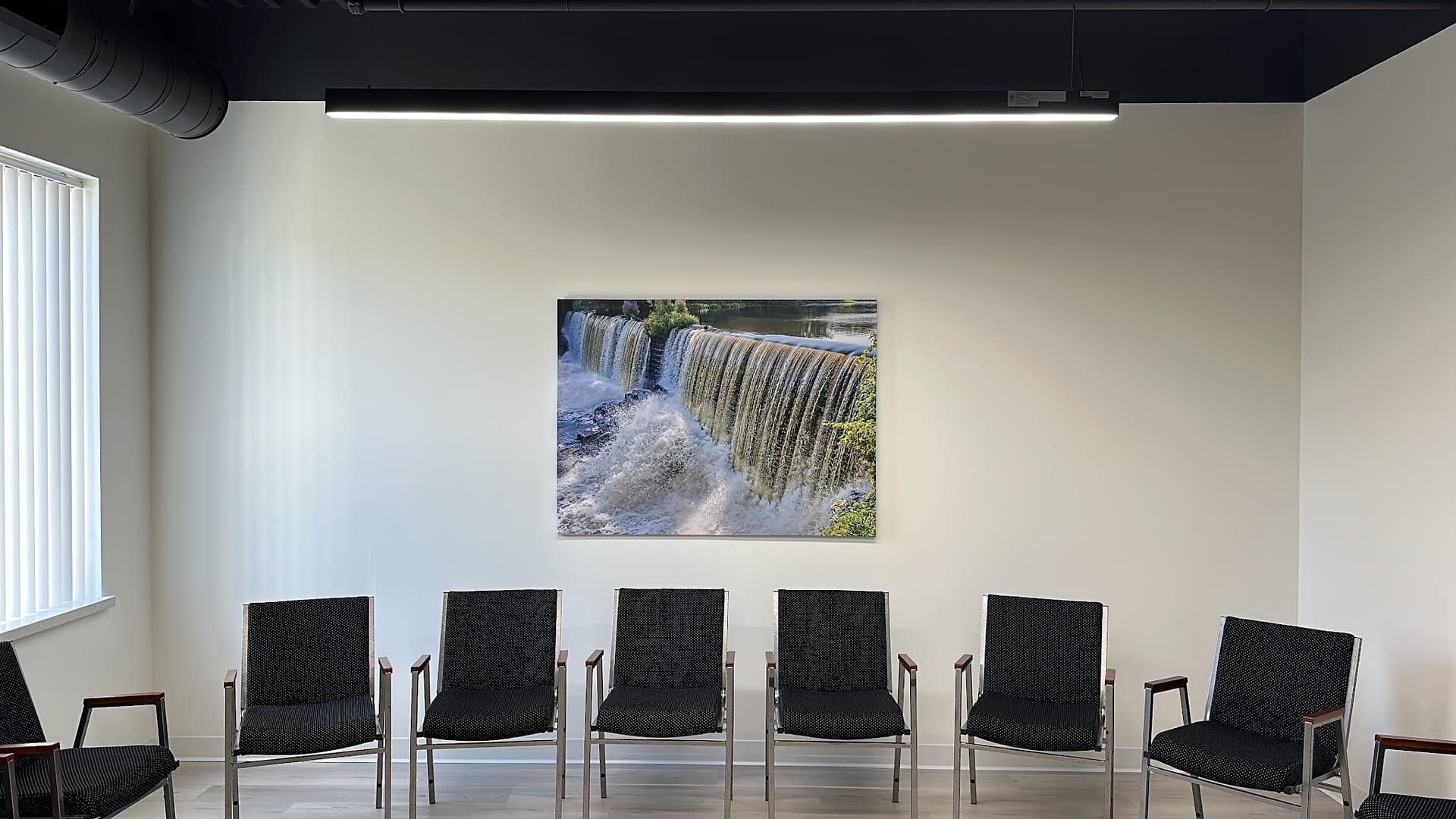 Clean waiting room with black chairs and waterfall artwork on white wall