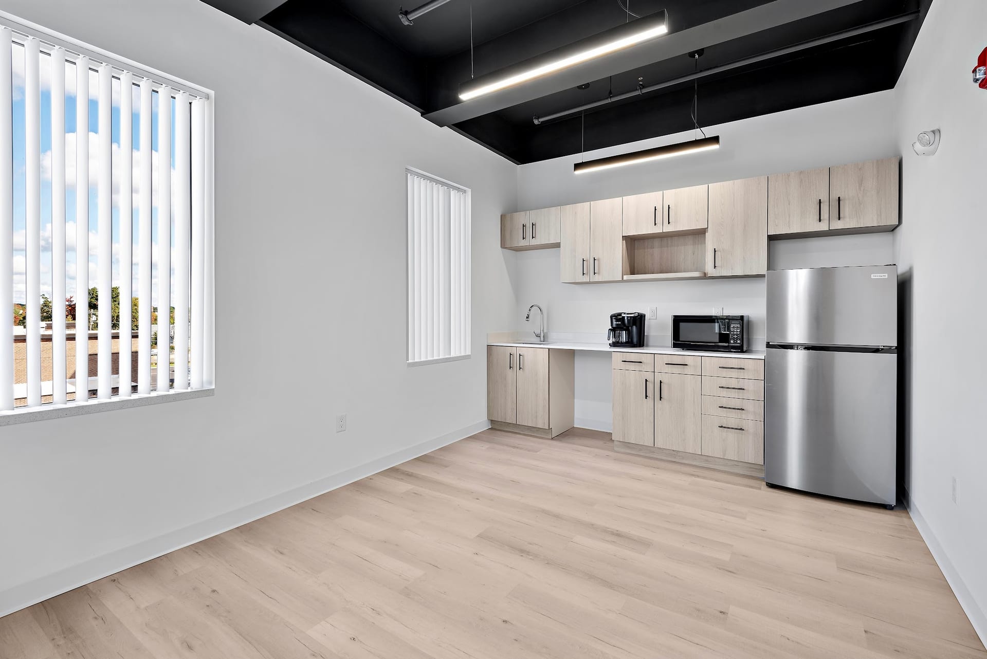 Modern break room kitchenette with light wood cabinets and stainless steel refrigerator