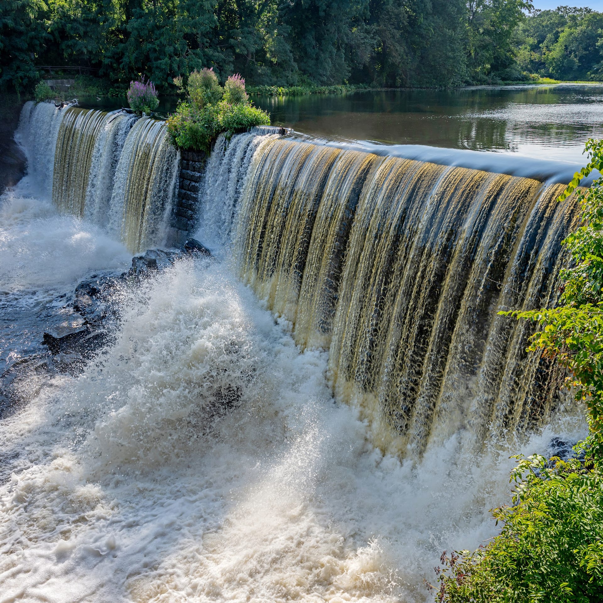 Powerful waterfall cascading over wide stone dam into churning river