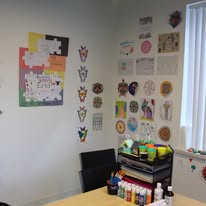 Art therapy room with colorful artwork displayed on walls and supply cart