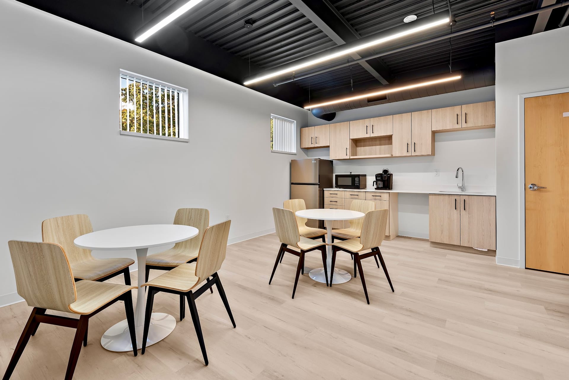 Modern patient lounge with round tables, wood chairs, and kitchenette